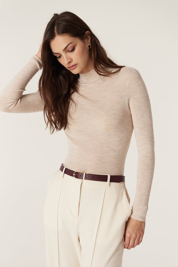 Woman wearing a slim genuine leather reversible belt in port with a gold buckle, styled with ecru pants.