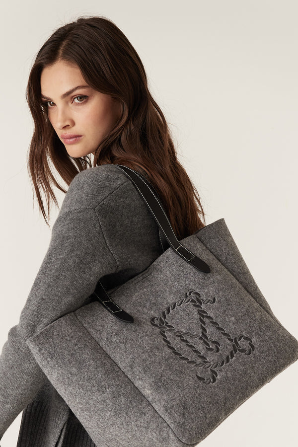 Woman carrying a charcoal marle wool blend felt travel tote with genuine leather handles and embroidered logo.