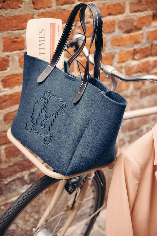 Indigo marle wool blend felt travel tote with genuine leather handles and embroidered logo, on a bicycle.