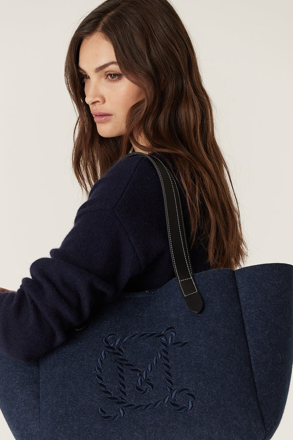 Woman carrying an indigo marle wool blend felt travel tote with genuine leather handles and embroidered logo.