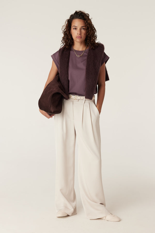 Woman in a berry Pima tee, cream wide-leg pants, and a dark brown fuzzy sweater draped over shoulders.