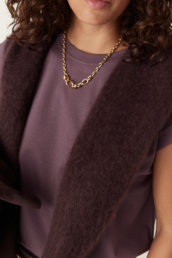 Close-up of a woman wearing a berry-colored Pima tee with a gold chain necklace and a dark brown fuzzy sweater draped over her shoulders.