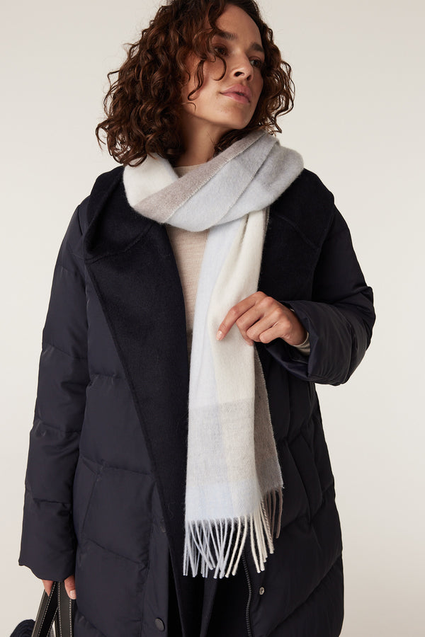 Woman wearing a soft pure wool scarf with blue, white, and beige checks, featuring fringed ends.