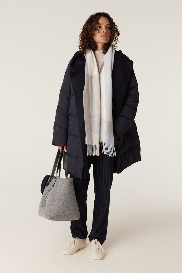 Woman wearing a blue check pure wool scarf, navy puffer coat, pinstripe pants, and carrying a grey felt tote bag.