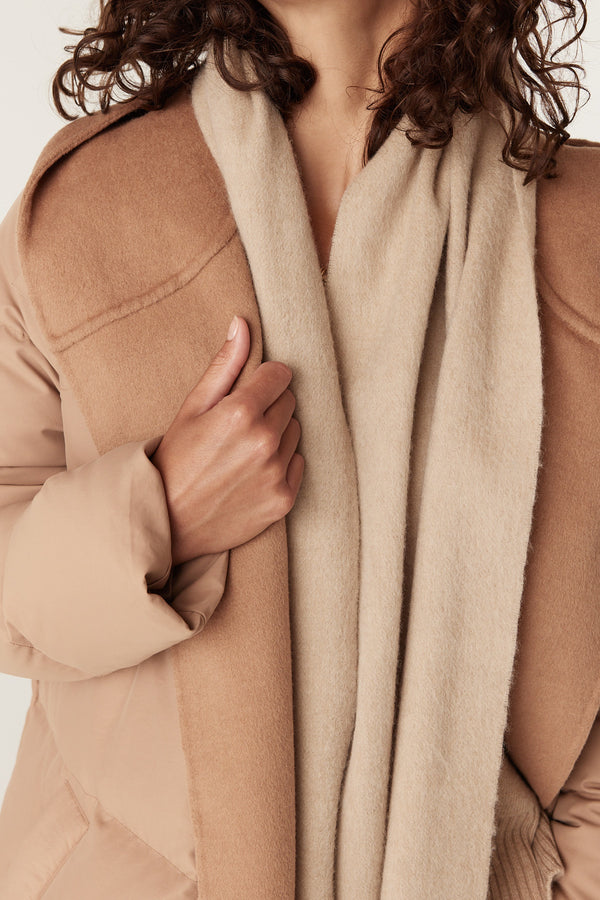 Soft camel pure wool scarf draped over a woman's neck, paired with a matching camel coat.