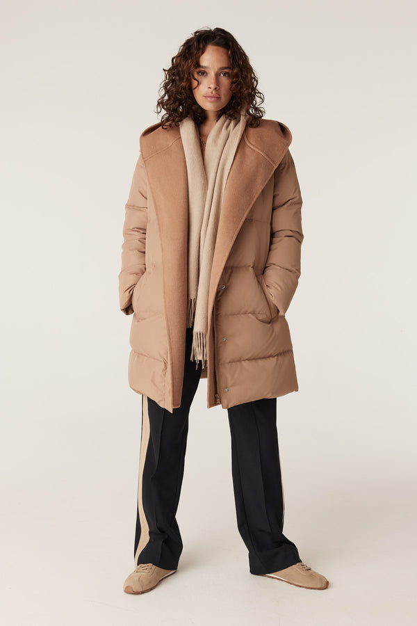 Woman wearing a camel pure wool scarf over a matching puffer coat, black pants, and sneakers.