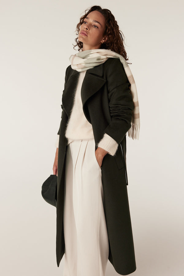 Woman wearing a sage check pure wool scarf, dark green coat, cream sweater, and light pants.