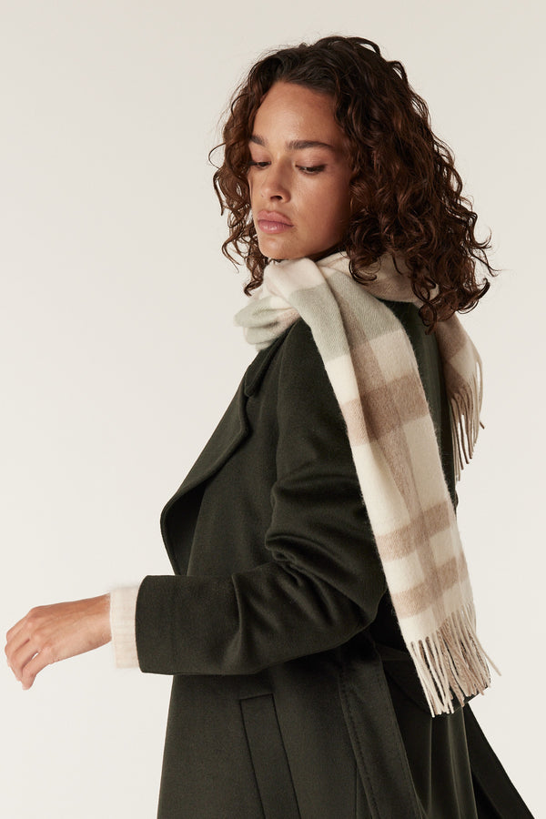 Woman wearing a sage check pure wool scarf with fringe, draped over a dark green coat.