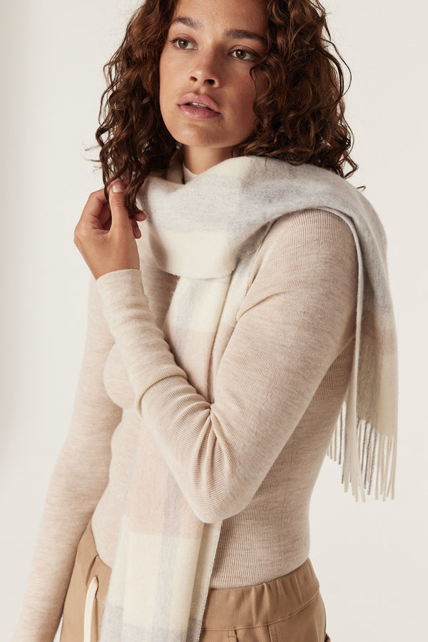 Woman wearing a soft blush check pure wool scarf with fringe, paired with a light long-sleeve top.