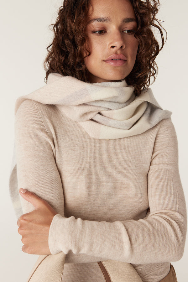 Woman wearing a blush check pure wool scarf, draped over a light beige long-sleeve top.