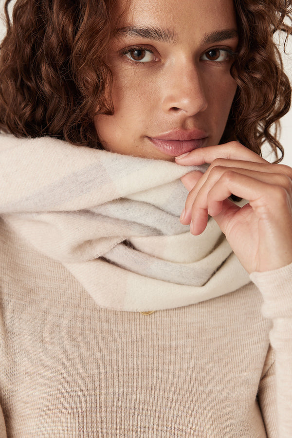 Woman wearing a soft pure wool blush check scarf and a light beige sweater.
