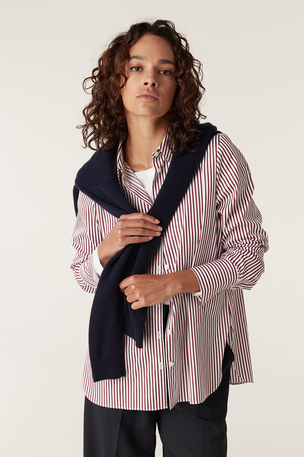 Woman wearing a red stripe Henri button-up shirt with a navy sweater draped over her shoulders.