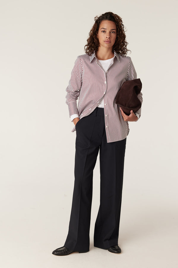 Woman wearing a red and white striped Henri shirt, black wide-leg trousers, and holding a brown bag.