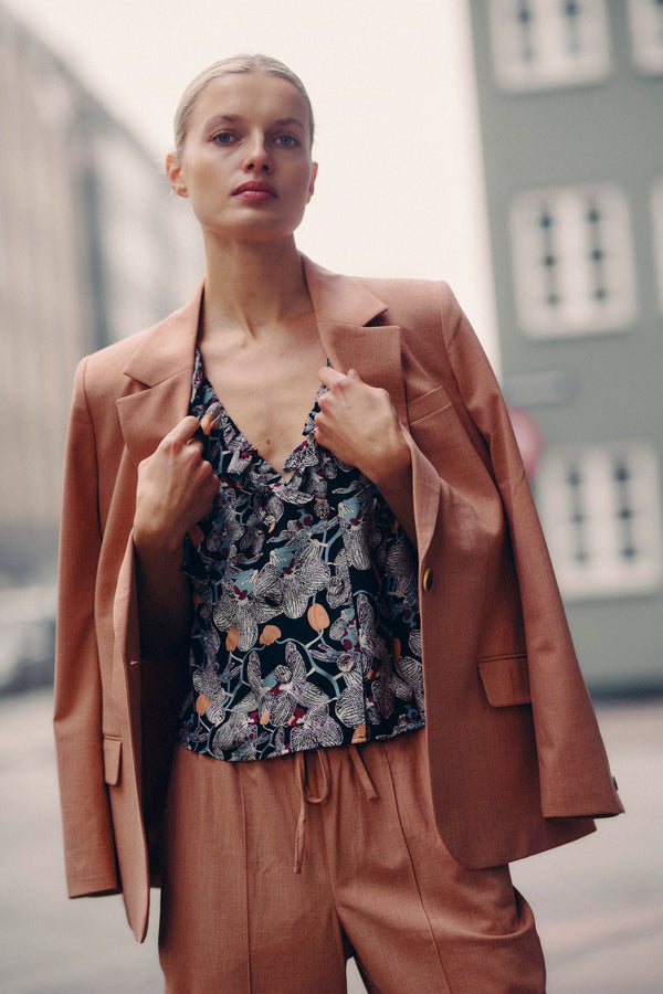 Model wears a Leigh Frill Top in Orchid Print silk blend, with a peach blazer and matching pants.