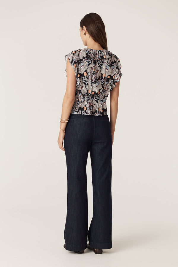 Woman from behind wearing a black silk blend Leigh Frill Top with an orchid print and dark wash jeans.
