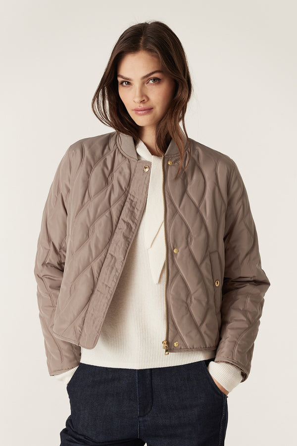 Woman wearing a fawn Martina Puffer jacket with quilted cable design, rib collar, and gold zipper.