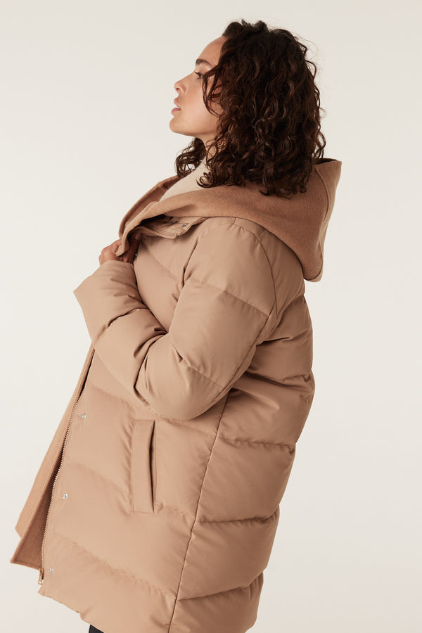 Woman in a camel Henderson puffer jacket with a wool-blend hood, side pockets, and a cozy, oversized fit.