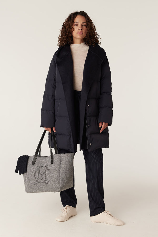 Woman wearing a navy Henderson Puffer coat with a cozy collar, holding a grey felt tote bag.