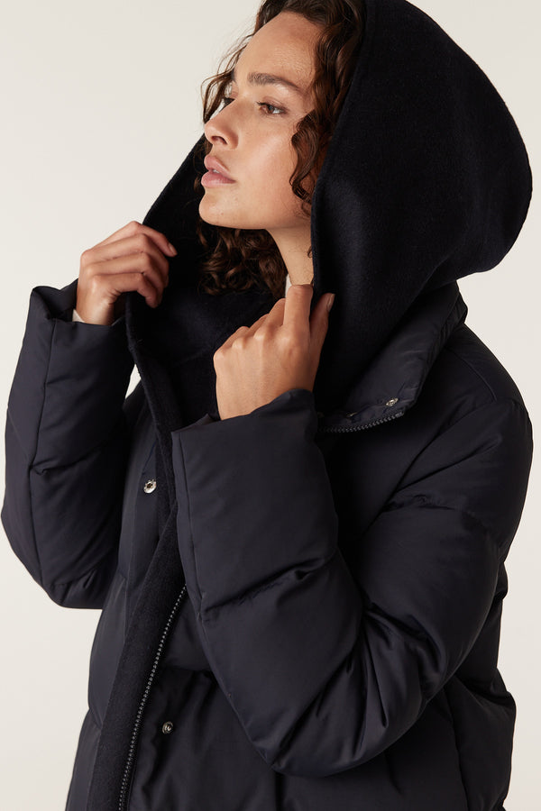 Woman wearing a navy Henderson puffer jacket with a large, soft hood and snap closures.