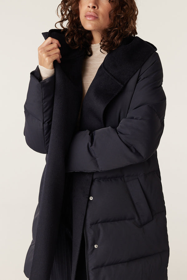 Woman wearing a navy Henderson Puffer coat with a contrasting black wool collar and lapel, and front pockets.