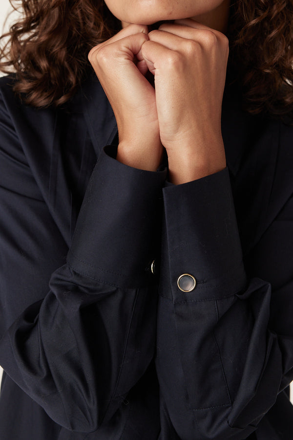 Navy Chester Pintuck Shirt with wide cuffs and gold buttons, worn by a person with hands clasped.
