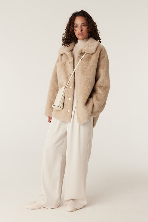 Franzi camel faux fur jacket with wide collar, gold buttons, and chest pocket, styled with cream pants.