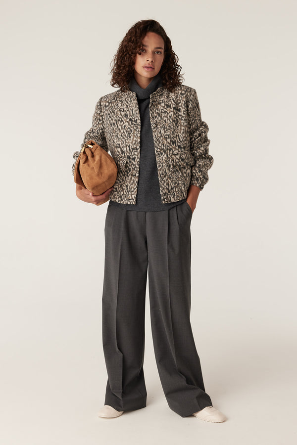 Woman in Heike Animal print jacket, grey turtleneck, wide-leg trousers, and brown clutch.