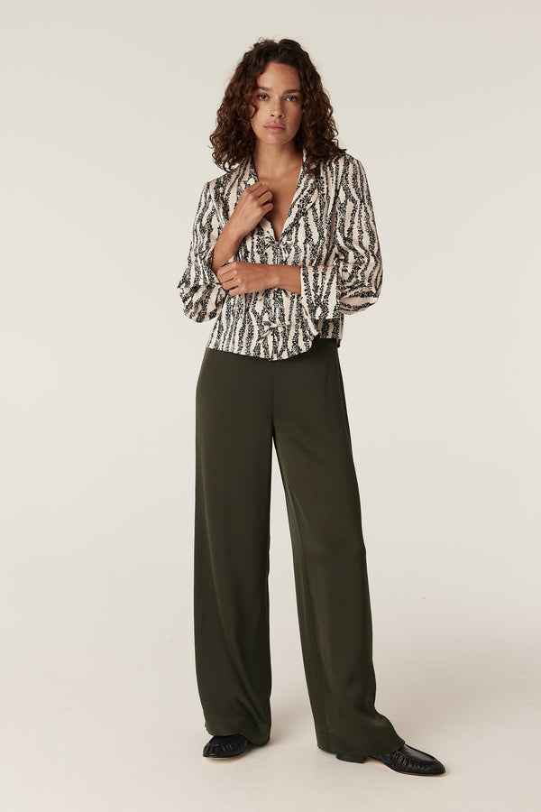 Woman in olive Sibelle wide-leg pants and a black and white patterned blouse.