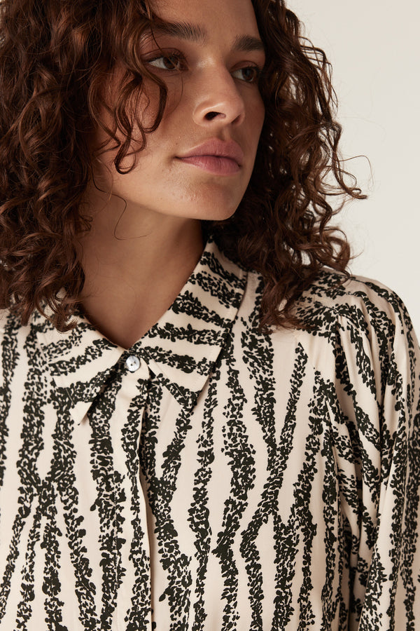 Woman wearing a cream Colette dress with a green speckle print, collared neckline, and button-front.