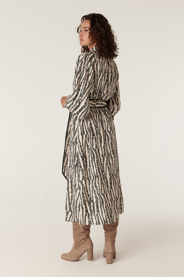 Woman in a long-sleeved Colette Speckle Print midi dress with a tie waist, paired with taupe boots.
