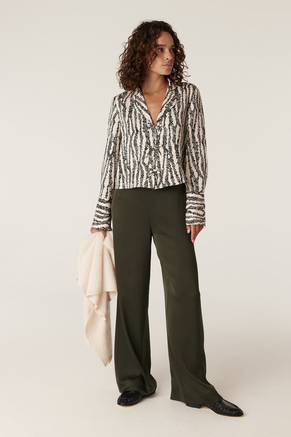 Woman in Sabine Blouse, a black and white speckle print long-sleeve top, with olive wide-leg pants.