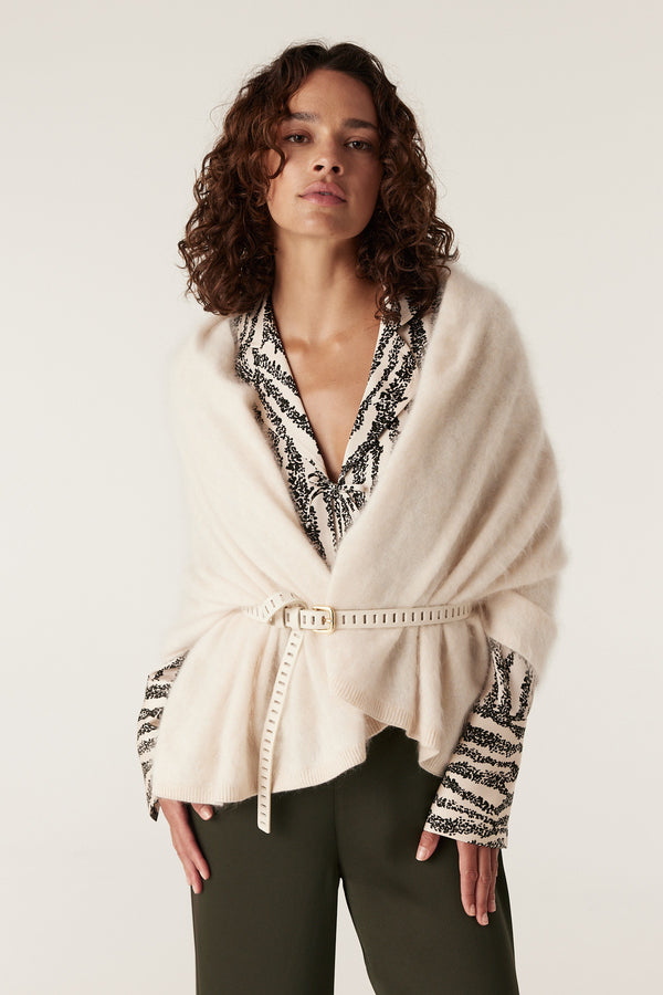 Woman in Sabine Blouse, a black and white speckle print top, under a cream knit wrap belted at the waist.