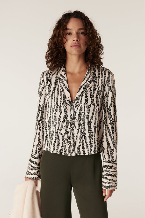 Woman in Sabine Blouse: black and white speckle print, long sleeves, collared v-neck, with olive pants.
