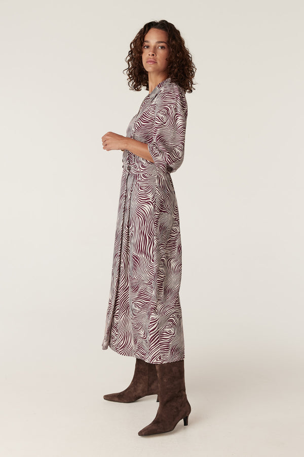 Woman in Anouk zebra print midi dress with long sleeves, belted waist, and brown suede boots.