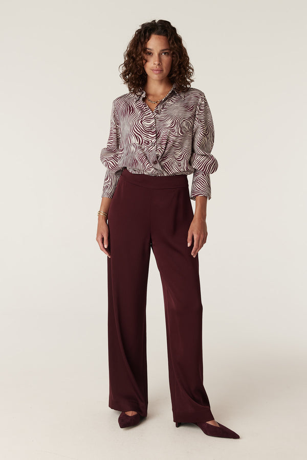 Woman in a Muse Blouse: zebra print, long-sleeve, collared, with burgundy wide-leg pants.