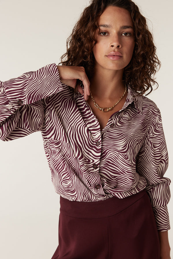 Woman in a long-sleeve Muse Blouse with a maroon and cream zebra print, paired with maroon pants.