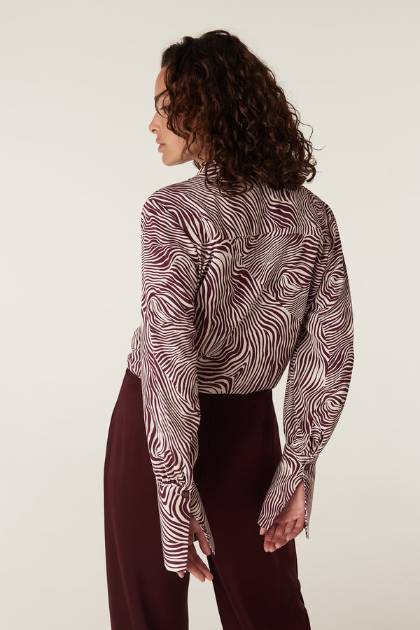 Woman in a long-sleeve Muse Blouse with a maroon and cream zebra print, paired with maroon pants.