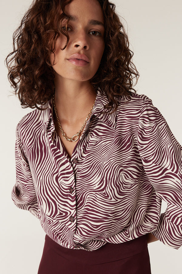 Woman wearing a Muse Blouse: burgundy and white zebra print, long-sleeved, collared, button-front.