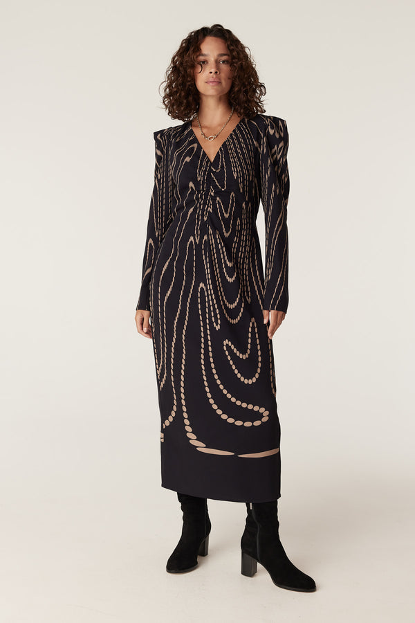 Woman in a navy camel spot Margaux dress with long sleeves, V-neck, and black boots.