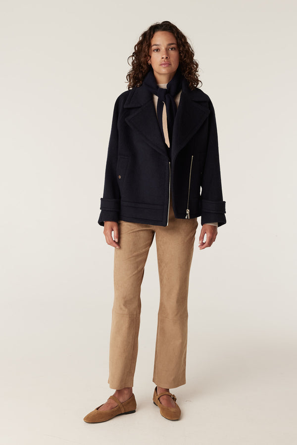 Navy Roy Jacket with wide lapels and silver zipper, worn by a woman with a striped scarf and tan pants.