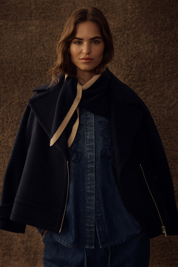 Woman in a navy Roy jacket, denim shirt with embroidery, and a beige striped scarf.