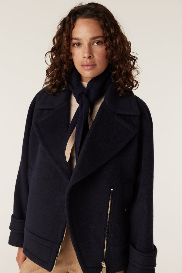 Woman wearing a navy wool Roy jacket with wide lapels, gold zipper detail, and a navy and beige scarf.