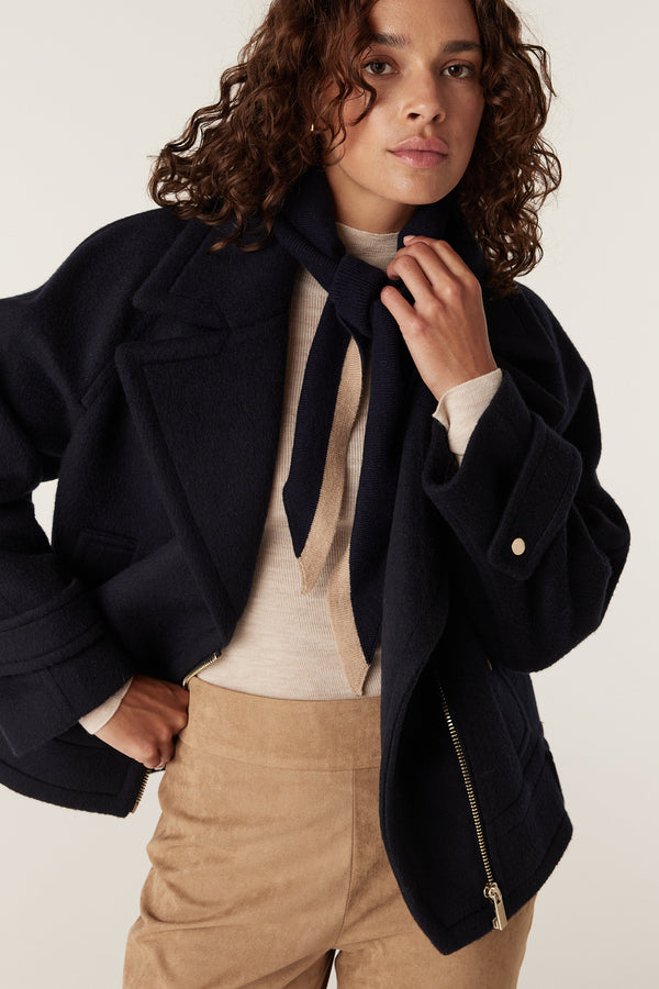 Navy wool Roy jacket with wide lapels, worn over a cream top and tan suede pants.