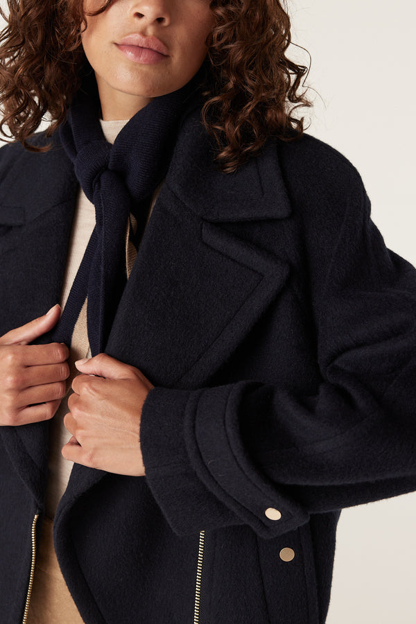 Woman in navy wool Roy jacket with wide lapels, gold buttons, and a matching scarf.