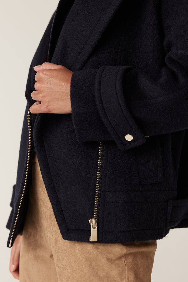 Navy Roy Jacket, a textured wool blend with gold zipper and snap details, worn over tan pants.