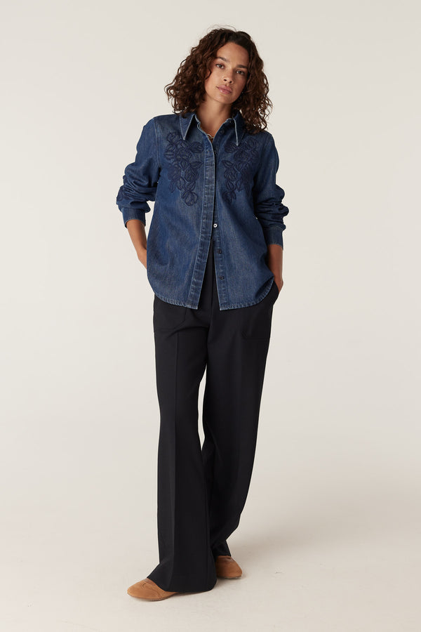 Model wearing an indigo denim shirt with floral embroidery and dark wide-leg pants.