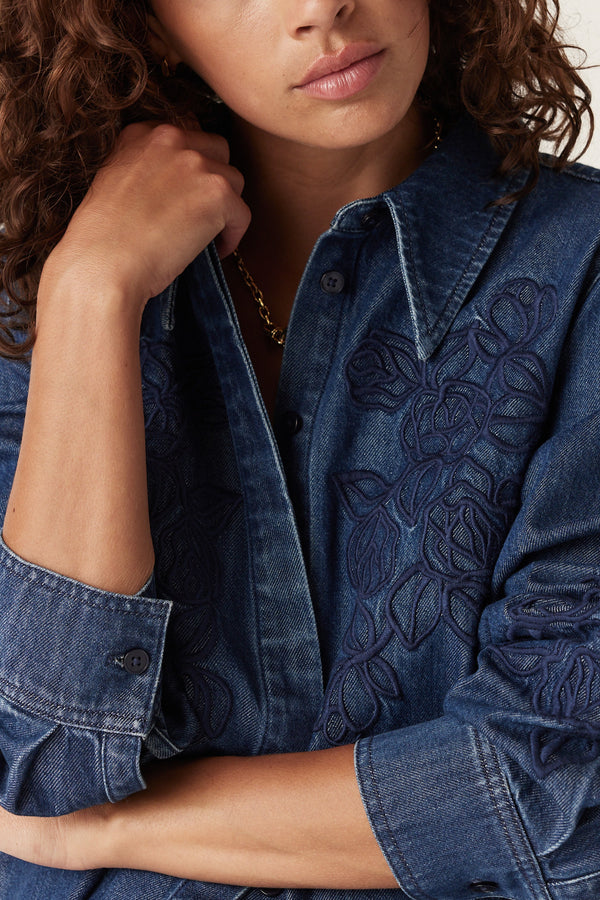 Indigo denim shirt with intricate dark blue floral embroidery, long sleeves, and a classic collar.