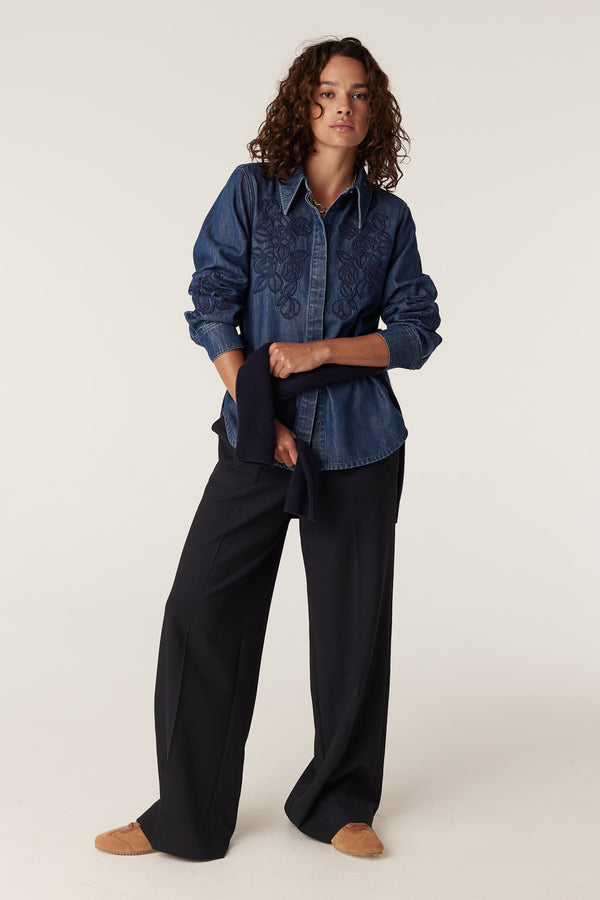 Indigo denim shirt with intricate floral embroidery, styled with black wide-leg pants.