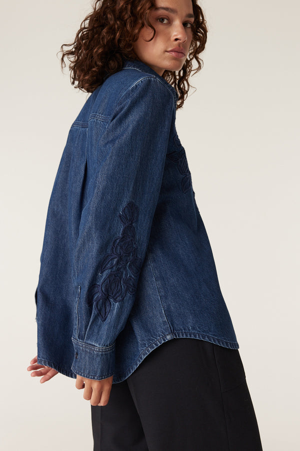 Essie indigo denim shirt with intricate floral embroidery on the sleeve, worn by a woman.