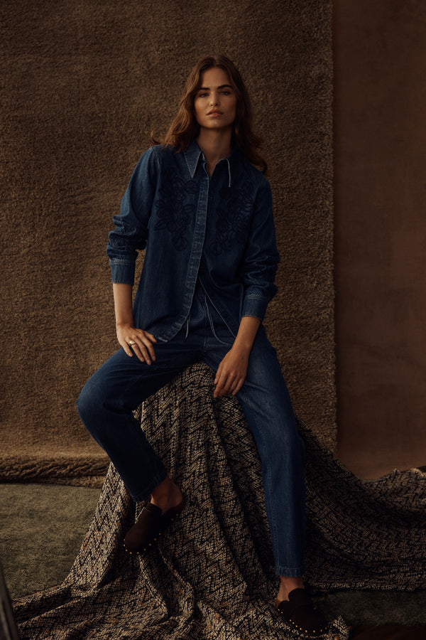 Woman wearing an indigo denim shirt with embroidery and matching denim jogger pants, dark mules.